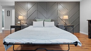 A modern bedroom with a large bed, two bedside tables, and a wall with geometric paneling. - Sweet Spot on Spence – Family Getaway - Walking distance to the excitement of Lambeau (Green Bay)