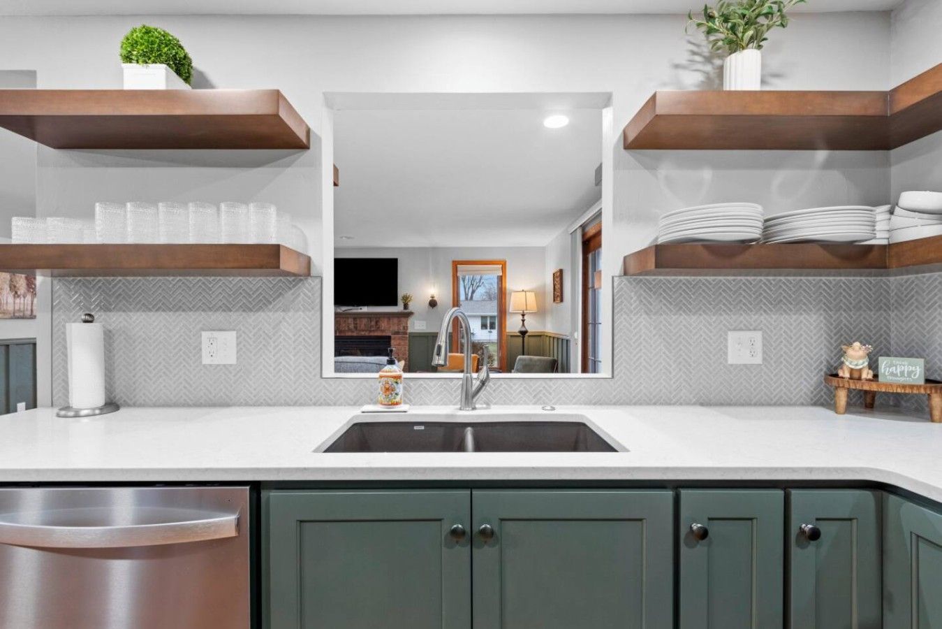 A modern kitchen with a central island, stainless steel sink, and green cabinets.