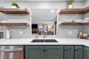 Een moderne keuken met een centraal kookeiland, een roestvrijstalen spoelbak en groene keukenkastjes.