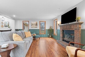 A living room with a fireplace, a sofa, a television, and a dining area.