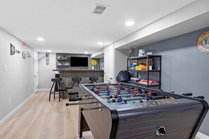 Una habitación con mesa de fútbol, zona de bar y espacio de estar con taburetes.