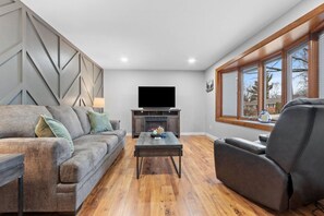 Una sala de estar con sofá, sillón, mesa de centro, televisor y chimenea.