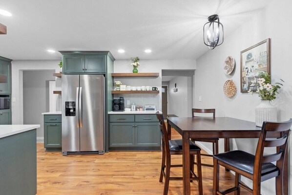 A modern kitchen with a stainless steel refrigerator, wooden dining table, and green cabinets.
