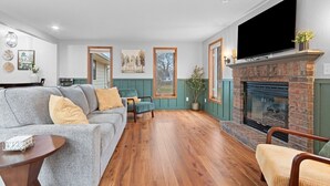 A living room with a fireplace, a sofa, a chair, and a television. - Sweet Spot on Spence – Family Getaway - Walking distance to the excitement of Lambeau (Green Bay)