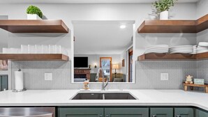 A modern kitchen with a central island, stainless steel sink, and green cabinets. - Sweet Spot on Spence – Family Getaway - Walking distance to the excitement of Lambeau (Green Bay)