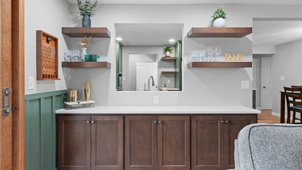 A modern kitchen with dark wooden cabinets, a white countertop, and built-in shelves with decorative items. - Sweet Spot on Spence – Family Getaway - Walking distance to the excitement of Lambeau (Green Bay)