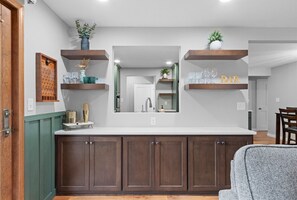 A modern kitchen with dark wooden cabinets, a white countertop, and built-in shelves with decorative items. - Sweet Spot on Spence – Family Getaway - Walking distance to the excitement of Lambeau (Green Bay)