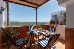 A balcony with a table set for four, chairs with striped cushions, a view of the countryside, and a brick oven. - Comeback Unforgettable (Salobreña)