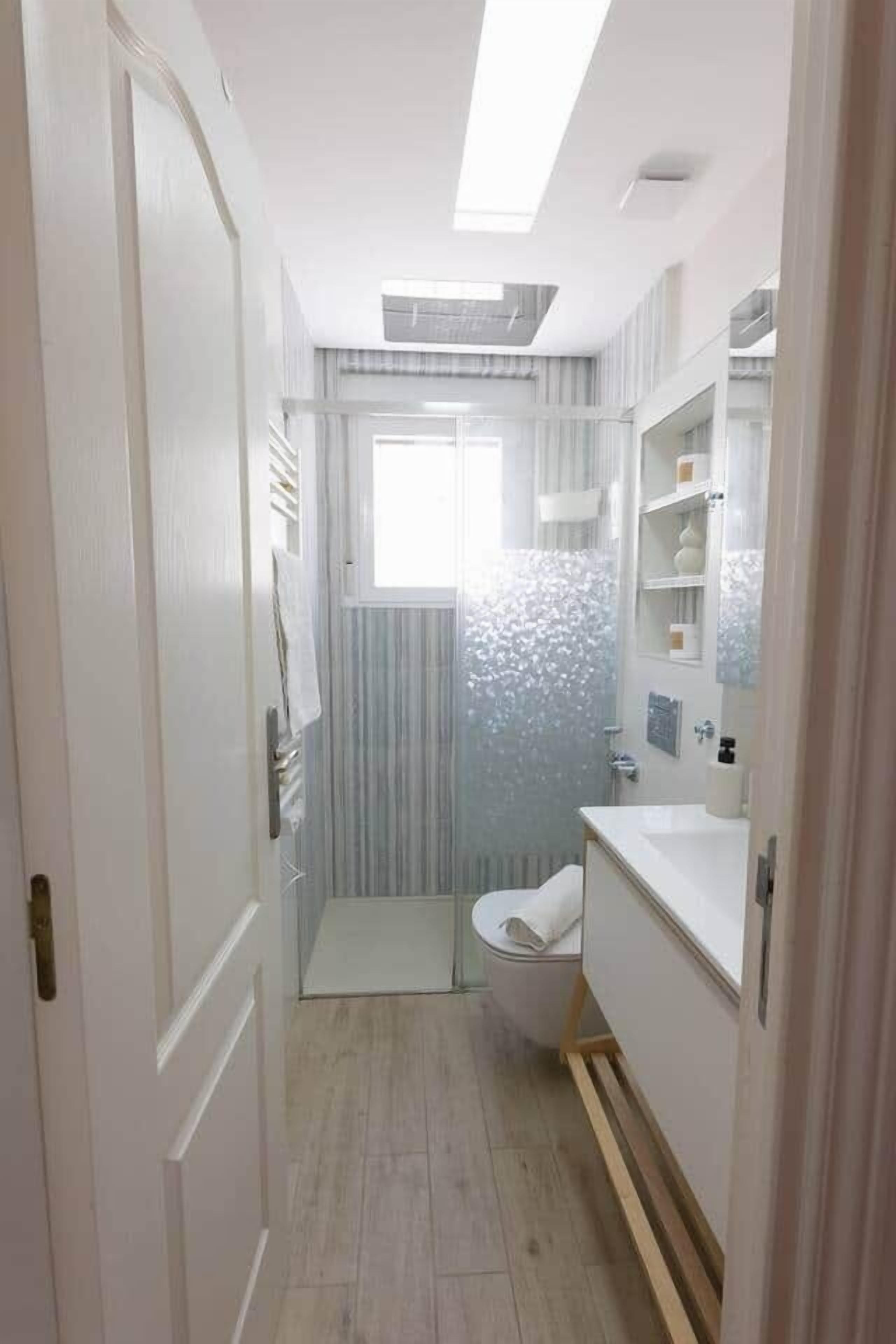 Ein schmales Badezimmer mit Toilette, Waschbecken und Duschbereich.
