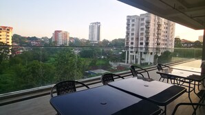 A balcony with tables and chairs, overlooking a cityscape with buildings and greenery. - Sam's Vacation @ The Straits Suite Residence formerly Ramada Suite by Wyndham (Johor Bahru)