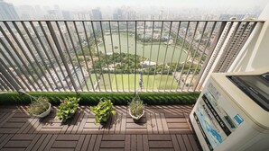 A balcony with a view of a cityscape, a water body, and two potted plants. - HN ETH Vinhomes D'capitale Resident (Hanoi)