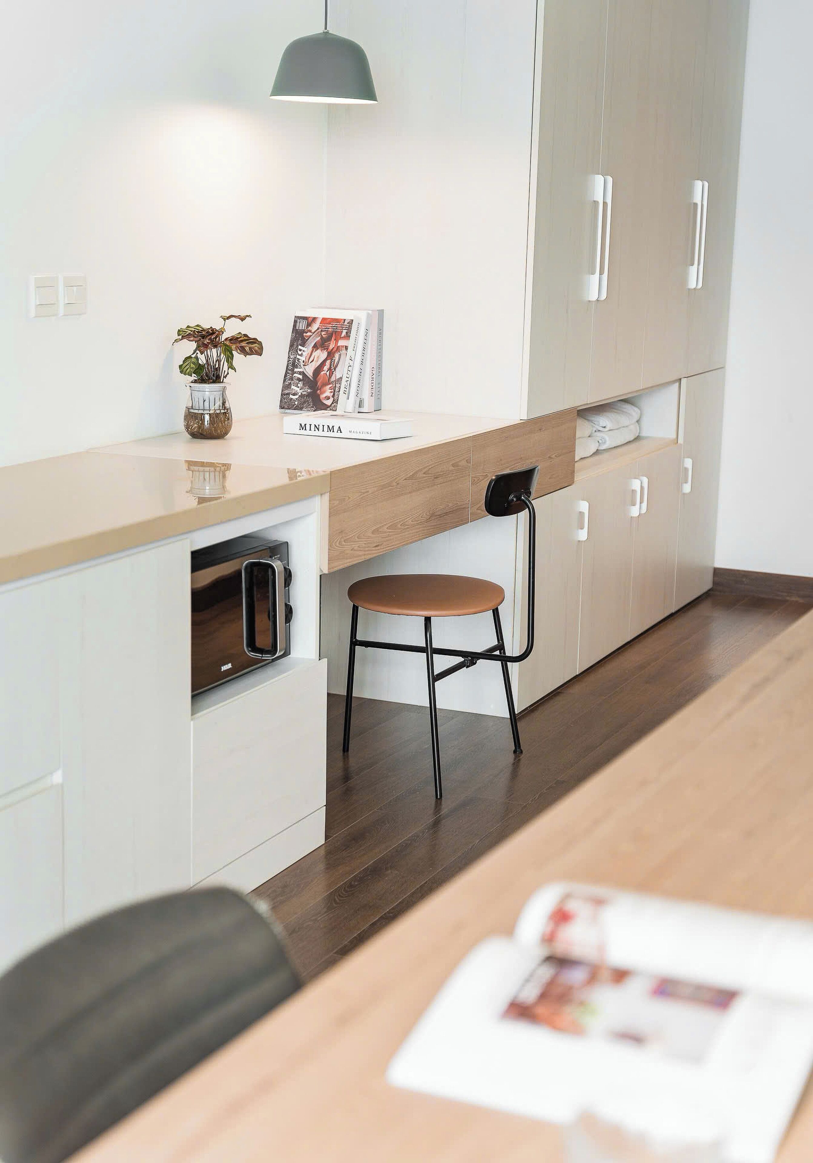 A modern kitchen with a wooden countertop, a built-in oven, a hanging light, and a dining area with a chair and table.
