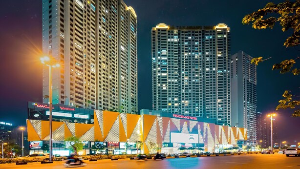 A high-rise building with multiple floors, a prominent entrance, and a large illuminated sign. - HN ETH Vinhomes D'capitale Resident (Hanoi)