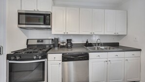 A kitchen with white cabinets, a microwave, a stove, a dishwasher, and a coffee maker. - Boho Westside Retreat | Fire Pit + Walk to Eats (Atlanta)