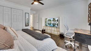 A bedroom with a bed, a desk, a chair, a ceiling fan, and a TV. - Boho Westside Retreat | Fire Pit + Walk to Eats (Atlanta)