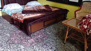 A room with a bed, a chair, a ceiling fan, and a window with blinds. - Hotel New Green view-apart (Srinagar)
