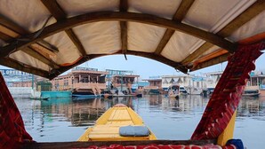 A boat with a red and white patterned cover, a yellow boat in front, and buildings in the background. - Hotel New Green view-apart (Srinagar)
