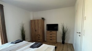 A bedroom with a bed, wooden wardrobe, TV, and potted plants. - FeWo Foorden Wohnglück 3 (Hesel)