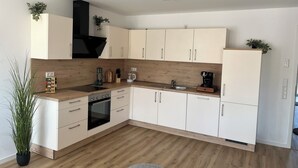 A modern kitchen with white cabinets, a black range hood, and wooden countertops. - FeWo Foorden Wohnglück 3 (Hesel)