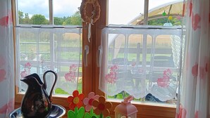 Un interior de madera con vistas por una ventana, una jarrón, un cuenco y un farol sobre una mesa.