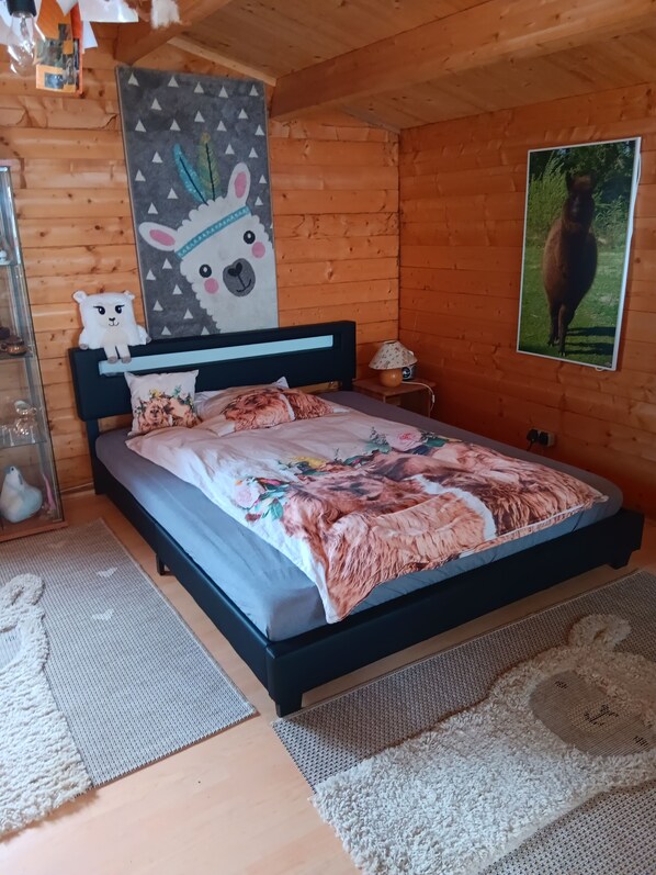 A cozy wooden room with a bed, a wall-mounted lamp, and a framed picture of a llama.