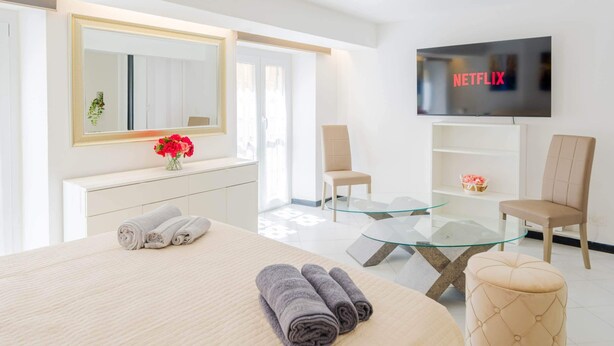 Una camera d'albergo moderna con un letto, un tavolino in vetro, una TV a parete e una poltrona.