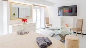 A modern hotel room with a bed, a glass coffee table, a TV mounted on the wall, and a chair. - CASA BEDA in the Borgo (Chiavari)