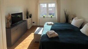 Een slaapkamer met een bed, televisie, bureau en raam met gordijnen.