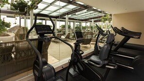 Ein Fitnessraum mit Ergometer und Laufband, großen Fenstern und Außenbereich mit Sitzgelegenheiten.