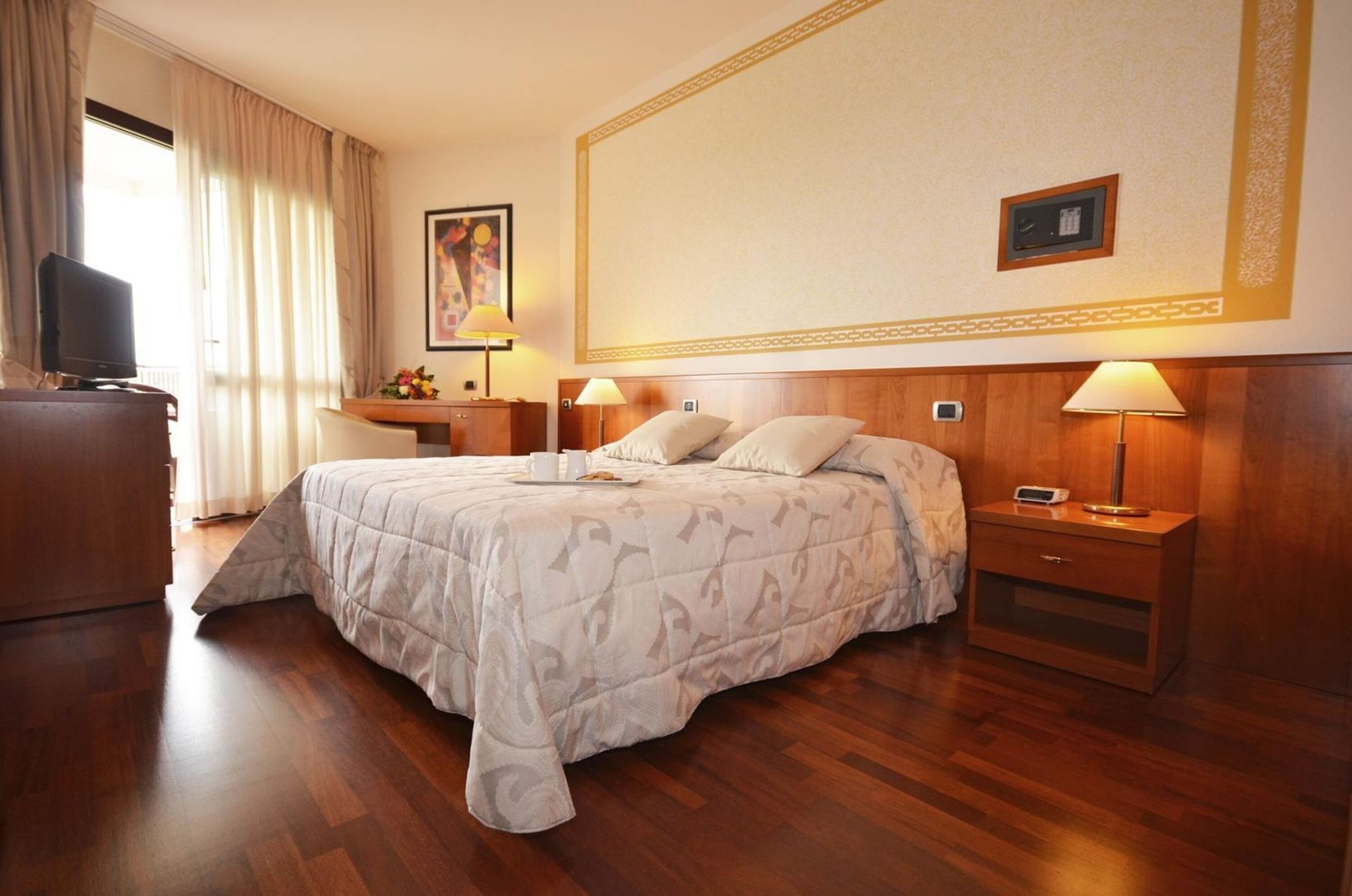 Ein Hotelzimmer mit Bett, Nachttischen, Schreibtisch, Fernseher und einem Fenster mit Vorhängen.