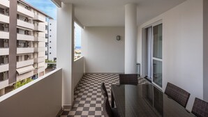 Un balcon doté d’un sol à carreaux, une table à manger avec des chaises, et une vue sur la mer.