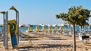 Een strand met ligbedden, parasols en een speelconstructie.