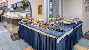 Een buffetopstelling met diverse gerechten en dranken, een koffieapparaat en een koelkast op de achtergrond.