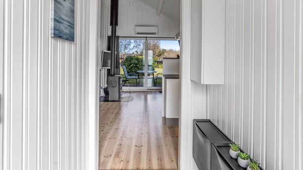Un pasillo con piso de madera que conduce a una cocina con estufa, una mesa de comedor y sillas. Hay plantas en macetas sobre una estantería.