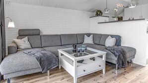 Una sala de estar moderna con un sofá modular, una mesa de centro de vidrio y una pared de ladrillo blanco.