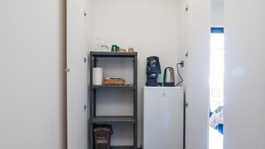 A narrow hallway with a dark wooden floor, white walls, and a small kitchenette area with a refrigerator, coffee maker, and shelves. - Santa Chiara in the city centre (Napoli)