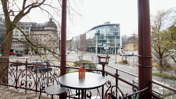 Een balkon met een tafel en stoel, met uitzicht op een straat met gebouwen en auto's.