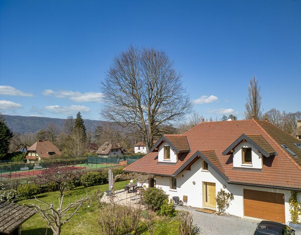 A residential area with houses, a tennis court, and a large tree. - Villa Norton - piscine et proche du Lac (Menthon-Saint-Bernard)