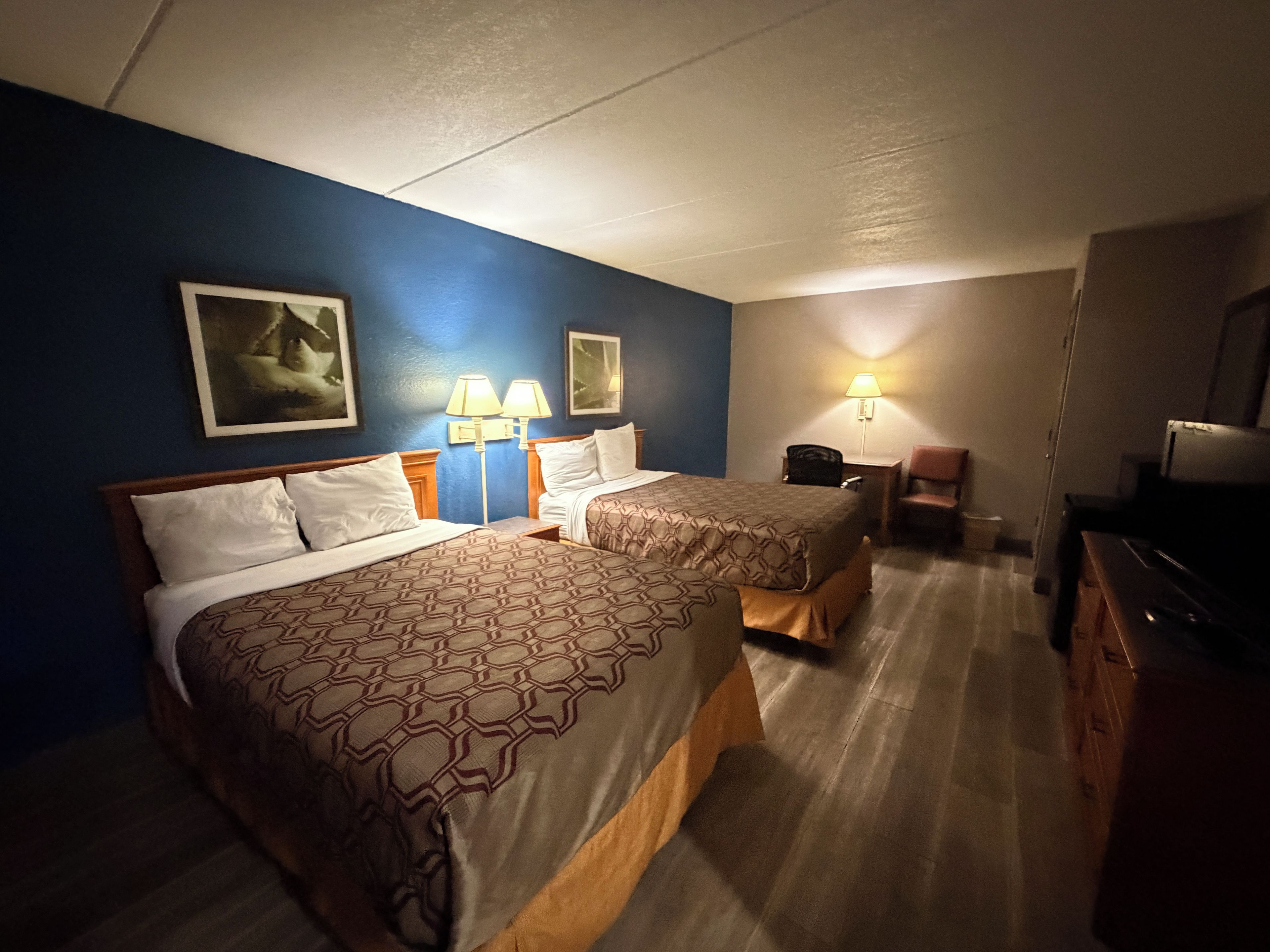 Ett hotellrum med två sängar, ett skrivbord, en stol, en TV och två väggmonterade lampor.