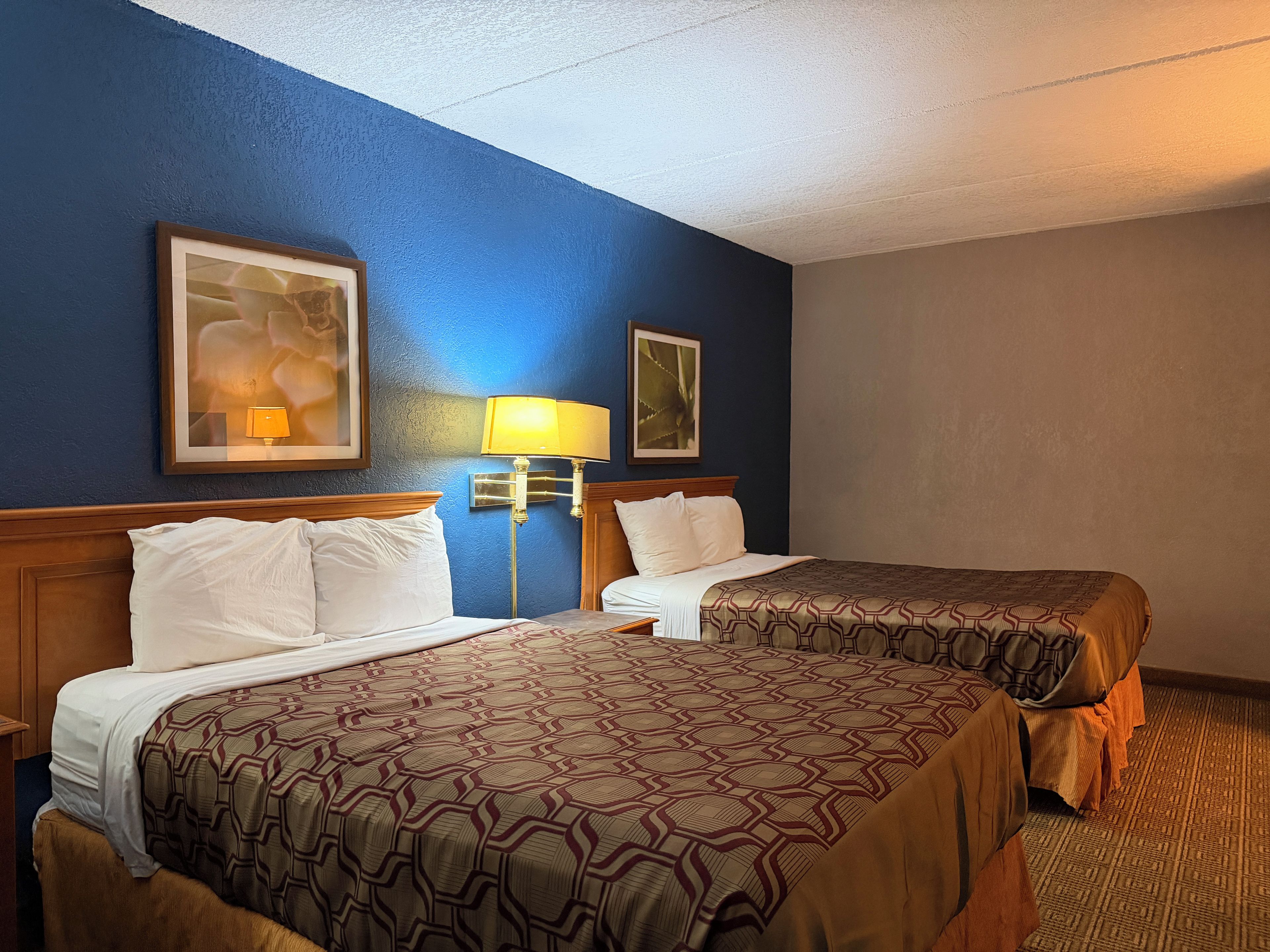 A hotel room with two beds, a nightstand, a lamp, and framed artwork on the walls.