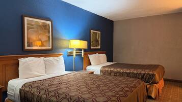 Habitación de hotel con dos camas, una mesita de noche, una lámpara y cuadros en las paredes.