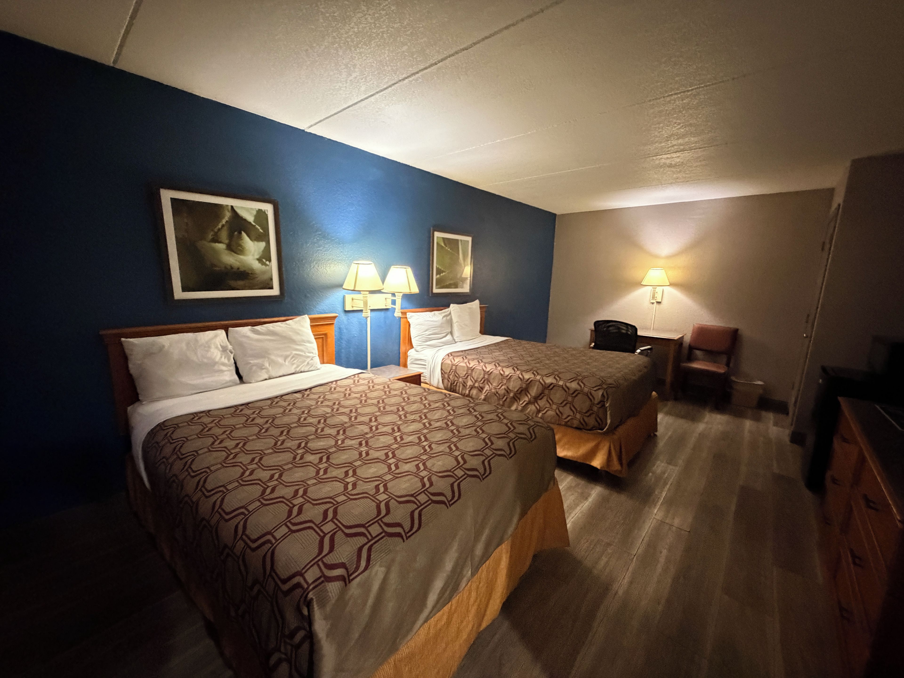 Ein Hotelzimmer mit zwei Betten, einem Schreibtisch, einem Stuhl und einer Lampe.