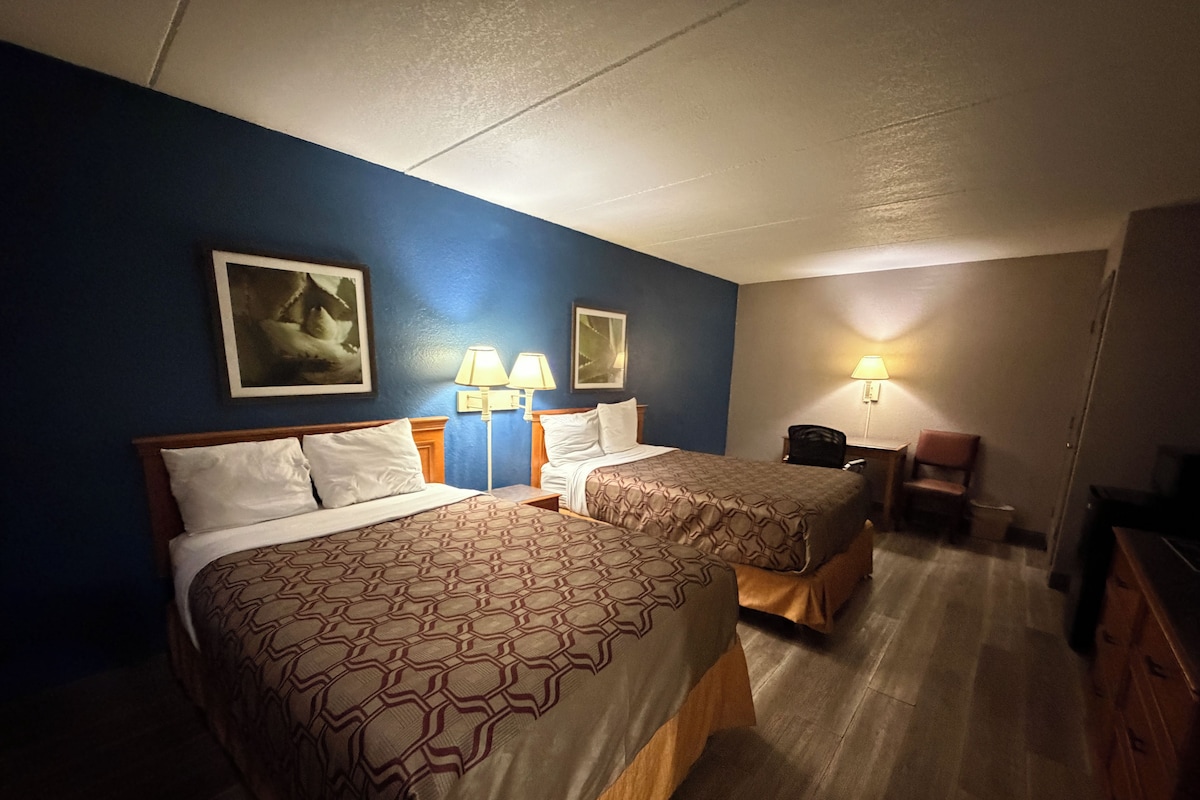 Una habitación de hotel con dos camas, un escritorio, una silla y una lámpara.