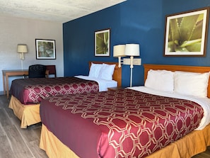 A hotel room with two beds, a desk, a chair, and two wall-mounted lamps.