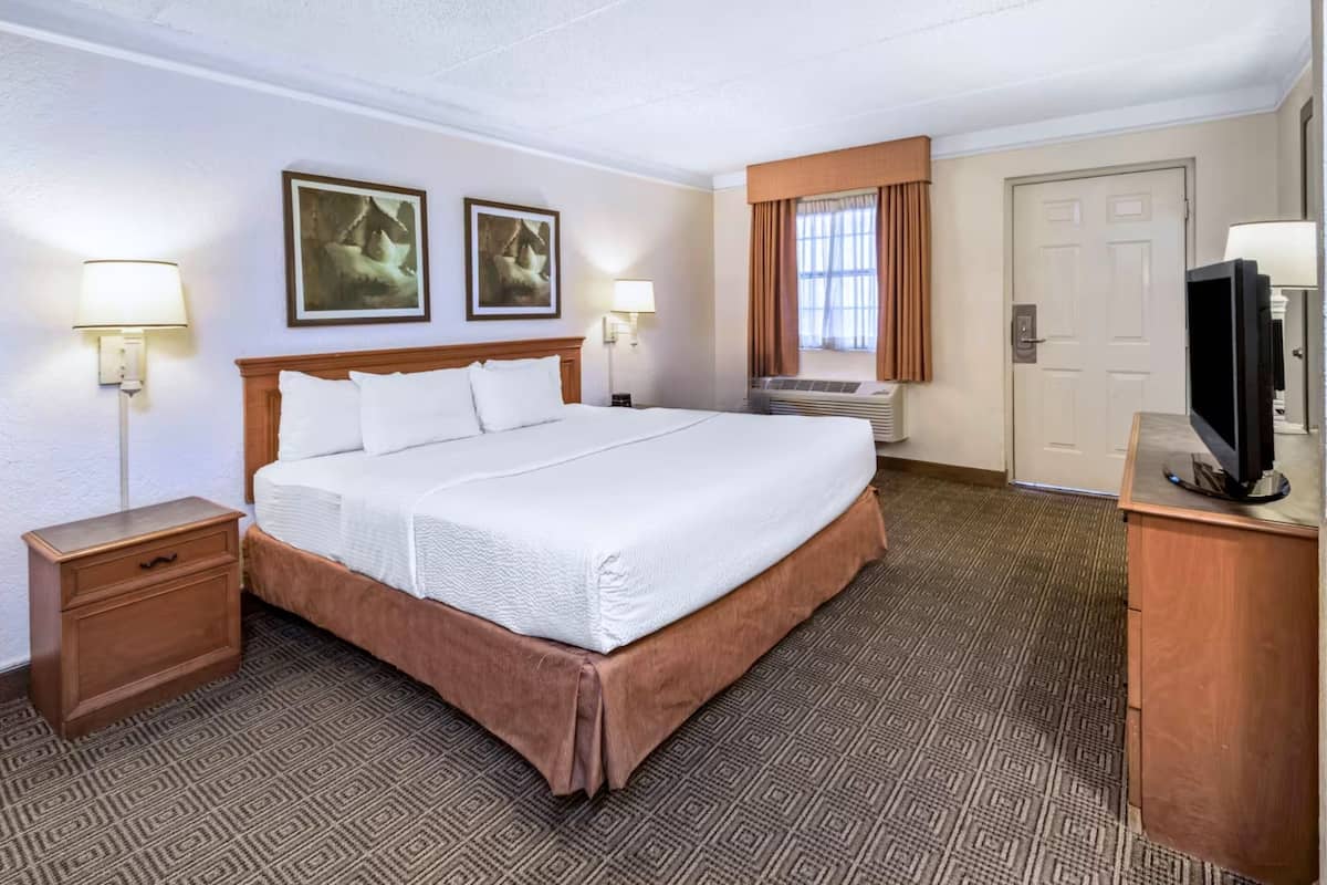 Quarto de hotel com uma cama grande, duas mesas de cabeceira, uma televisão e uma porta.