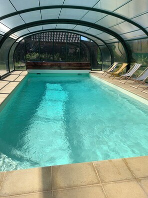 A swimming pool with a glass ceiling, surrounded by lounge chairs and a wooden deck. - Chic & Charme Cottage (Suzay)
