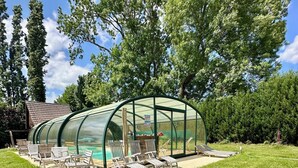 A glass-enclosed outdoor pool area with lounge chairs and a wooden deck. - Chic & Charme Cottage (Suzay)