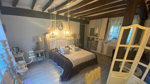 A bedroom with a large bed, bedside tables, a dresser, a mirror, and a window with curtains. - Chic & Charme Cottage (Suzay)