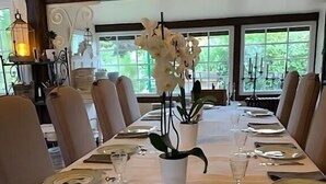 A dining table set for six with white tablecloths, plates, cutlery, and a vase of white flowers. - Chic & Charme Cottage (Suzay)