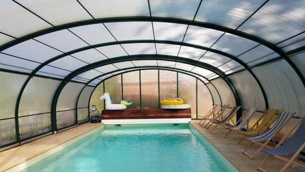 An indoor swimming pool with a glass ceiling, lounge chairs, and a wooden bench with a yellow and white object on it. - Chic & Charme Cottage (Suzay)